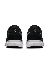Des chaussures de sport noires avec une tige en maille, une semelle blanche amortissante et un marquage distinctif sur le talon. La vue arrière met en valeur le design et les matériaux.