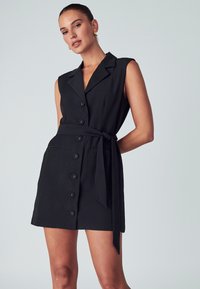 Vestito nero senza maniche con colletto, bottoni frontali e cintura legata in vita. Presenta tasche laterali e un orlo dritto e elegante.