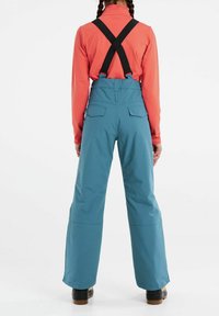 Blå skidbyxor med svarta justerbara hängslen, vida ben och två bakfickor. Bärs över en korallfärgad långärmad tröja. Hållbar tygkvalitet.