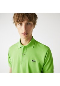 Ljusgrön polo med andningsbart tyg, med en krage med två knappar, korta ärmar och en svart broderad logotyp på bröstet.