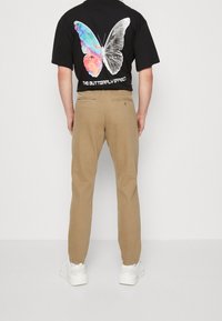 Maglietta nera con una grafica di farfalla colorata sul retro, abbinata a pantaloni beige e sneakers bianche. Vista posteriore.