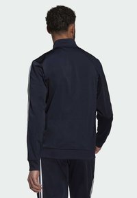 Chándal de entrenamiento azul marino con cuello alto, con franjas blancas a lo largo de los hombros y las mangas, fabricado con un tejido suave y ligero.