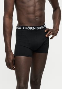 Ανδρικός κορμός με μαύρα μποξεράκια Björn Borg, χέρι στη μέση, πάνω σε απλό ανοιχτό φόντο.