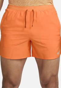 Nike juoksuhousut kirkkaassa oranssissa, valmistettu kevyestä kankaasta. Omistaa joustavan vyötärönauhan, jossa on naru ja pieni logo helman kohdalla.