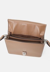 Koňakově hnědá kožená kabelka s pevnou konstrukcí, stříbrnými kovovými doplňky, dvěma vnitřními přihrádkami a kontrastním bílým prošíváním podél okrajů.