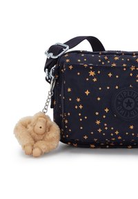 Navy fabric bag with golden star pattern, a zip closure, and a furry beige monkey keychain attached. Features an embossed logo on the front.