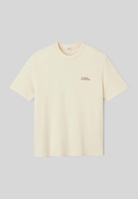 T-shirt en coton couleur crème à manches courtes et col rond. Comprend un petit texte "l'évolution est un processus" sur la zone du côté gauche de la poitrine.