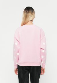 Rosa sweatshirts med blommönsterbroderi på ärmarna, rund halsringning och ribbade ärmar; bärs tillsammans med svarta kostymbyxor med smala ränder.