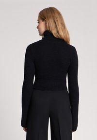 Czarny, prążkowany sweter z golfem, z długimi rękawami, wykonany z teksturowanej tkaniny. Krótkie uczucie widoczne z tyłu.