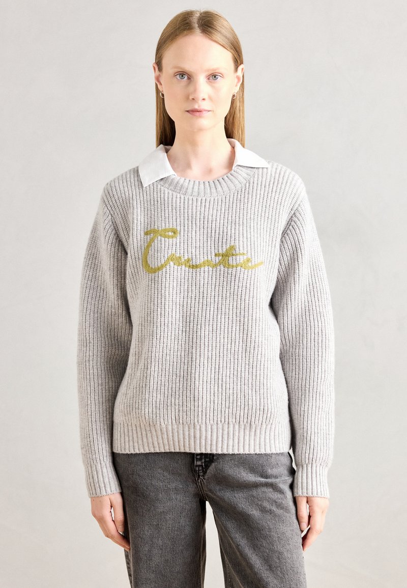 Gray ribbed sweater with a round neckline, featuring a gold cursive "Create" design on the front. Worn over a white collared shirt.
