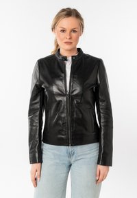 Zwarte leren jas met een hoge kraag, rits aan de voorkant en twee zijzakken. Het materiaal is soepel en aansluitend, gecombineerd met lichtblauwe jeans.