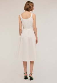 Rochie albă fără mâneci, cu un corset ajustat, fustă evazată și curea. Textură netedă, până la genunchi, design simplu și închidere cu fermoar la spate.