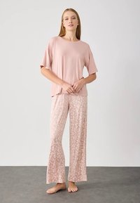 Šviesiai rožinė trumpomis rankovėmis palaidinė derinama su plačiomis pižamos kelnėmis, puošniomis minkštu, abstrakčiu leopardų raštu panašiomis spalvomis. Lygus paviršius.