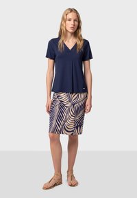 Top azul marino de manga corta con escote en V y detalles de pliegues, combinado con una falda de longitud hasta la rodilla que presenta un patrón de hojas crema sobre un fondo azul marino.