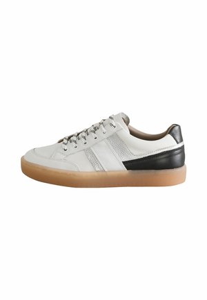 Sneaker en cuir blanc avec des accents noirs et gris, bout rond et côtés texturés. La semelle en caoutchouc beige et les lacets à motif complètent le design.