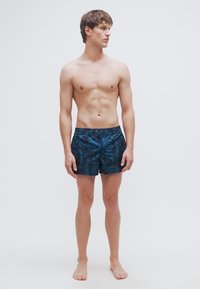 Μαγιό σορτς από μπλε ύφασμα με λουλουδάτο μοτίβο, διαθέτει ελαστική μέση με κορδόνι και δύο πλαϊνές τσέπες, με κανονική εφαρμογή.