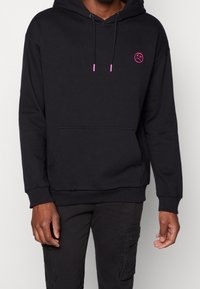 Svart hoodie i bomullsblandning, med dragsko i pink färg, framficka och en cirkulär pink grafisk bild på bröstet.