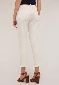 Pantalon en coton blanc avec une coupe slim, doté de deux poches arrière et d'un ourlet retroussé, associé à des sandales à talons bruns.
