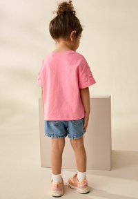 Roze T-shirt met korte mouwen en bloemenborduurwerk op de mouwen, gecombineerd met denim shorts en roze sneakers, gezien van achteren.
