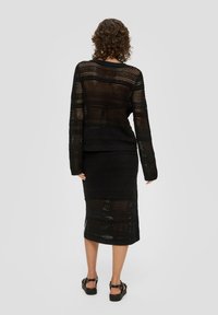 Czarny dziany zestaw składający się z bluzki z długim rękawem i spódnicy do kolan, z siateczkowym wzorem i ściągaczem na dole. Płaskie obuwie dopełnia stylizację.