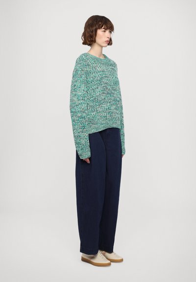 Loose-fitting turquoise sweater with textured knit, paired with dark blue wide-leg jeans and light-colored shoes.