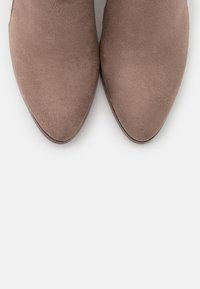 Een paar taupe suède schoenen met puntige neuzen, naast elkaar geplaatst op een witte achtergrond, bekeken vanuit boven.