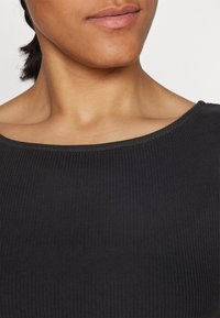 Top in tessuto nero a coste con scollatura ampia e superficie testurizzata. Il design presenta una finitura liscia e una leggera elasticità.