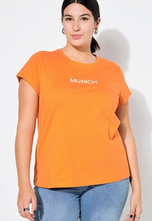 T-shirt arancione a maniche corte con il testo bianco "MUNICH" sul davanti. Tessuto in cotone morbido, taglio rilassato, scollatura rotonda e fessura laterale discreta.
