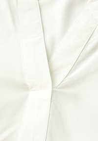 Tissu en coton blanc avec un détail de couture diagonal, présentant une texture lisse et un subtil éclat, dans un design en forme de V au niveau du col.