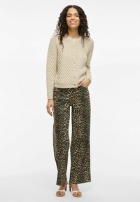 Cárdigan de textura beige con un patrón de diamantes, con botones plateados. Combinado con pantalones de pierna ancha de estampado de leopardo y tacones destalonados.
