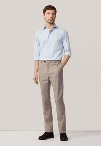 Camisa de rayas azul claro con mangas enrolladas, pantalones beige y zapatos marrones oscuros. Diseño sencillo con un botón en el frente y bolsillos.
