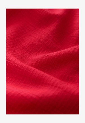 Roter Stoff mit einer strukturierten Oberfläche und einem Rautenmuster. Der Stoff ist weich und leicht reflektierend, wodurch die gleichmäßige Farbe betont wird.