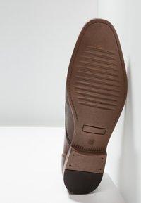 Sole di scarpa in pelle marrone con texture rigata e bordo liscio. Area di trazione in gomma nella parte anteriore. Etichetta della taglia visibile.