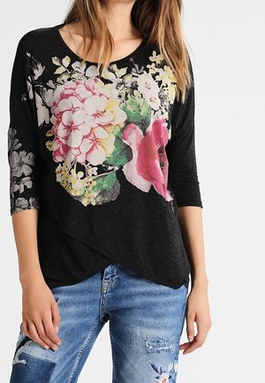 Sort top med trekvartærmer med blomstermønster i pink og hvid, kombineret med slidte blå jeans.