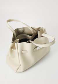 Lys beige lær totepose med en teksturert finish, som har to håndtak, et innvendig rom og et sølvfarget hardware-element.