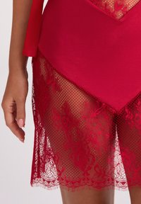 Czerwona sukienka z dopasowanym topem, koronkowymi wykończeniami i przezroczystą, siateczkową dolną częścią z kwiatowymi wzorami oraz falbankowanym dołem.