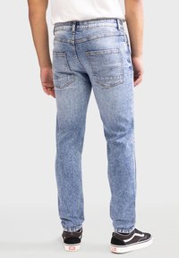 Vaqueros de mezclilla azul claro con corte recto, que presentan bolsillos traseros y una sutil textura de desvanecimiento. Llevados con zapatillas negras.