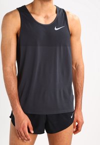 Débardeur de sport en mesh noir avec un col rond et le logo Nike en blanc. Caractérisé par un design léger et une coupe ajustée.