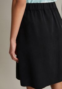 Schwarzer Rock mit elastischem Bund, der eine glatte Textur und einen geraden Schnitt aufweist. Der Saum ist leicht geschwungen.