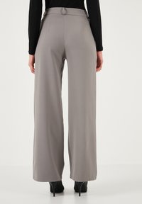 Wide-leg trousers in light gray fabric, featuring a high waistband, smooth texture, and minimal stitching details. Black heels visible.