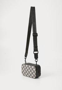 Zwarte en grijze rechthoekige tas met een voorzijde van een patroonstof. Voorzien van een zwarte schouderband met verhoogde letters en een ritssluiting.
