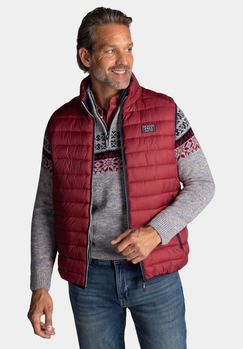 Rode puffer vest met hoge kraag, met een horizontaal gewatteerd ontwerp. Laagjes over een gemêleerd grijze gebreide trui met blauwe accenten.