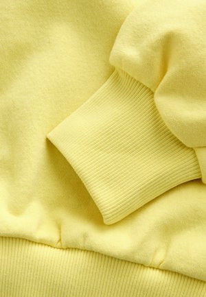 Yellow sweatshirt fabric with a soft, textured finish. Ribbed cuffs and waistband, featuring a seamless design for a smooth appearance.