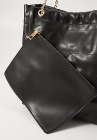 Sac à main en cuir matelassé noir avec une pochette plate amovible dotée d'une fermeture à glissière dorée et d'une bandoulière en chaîne pour une facilité de transport.