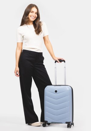 Valise de cabine de couleur bleu clair, avec un design en chevron texturé, des accents noirs, une poignée rétractable et quatre roues pour la mobilité.