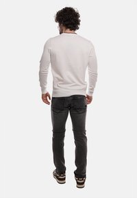 Maglione lavorato a maglia bianco con scollatura rotonda, abbinato a jeans slim-fit grigio scuro. Da notare è il tessuto texturizzato del maglione.