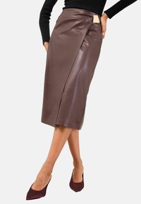 Gonna a matita in pelle marrone con design avvolto, caratterizzata da una spacco laterale e un piccolo dettaglio con etichetta in vita. Texture liscia, lunghezza media.