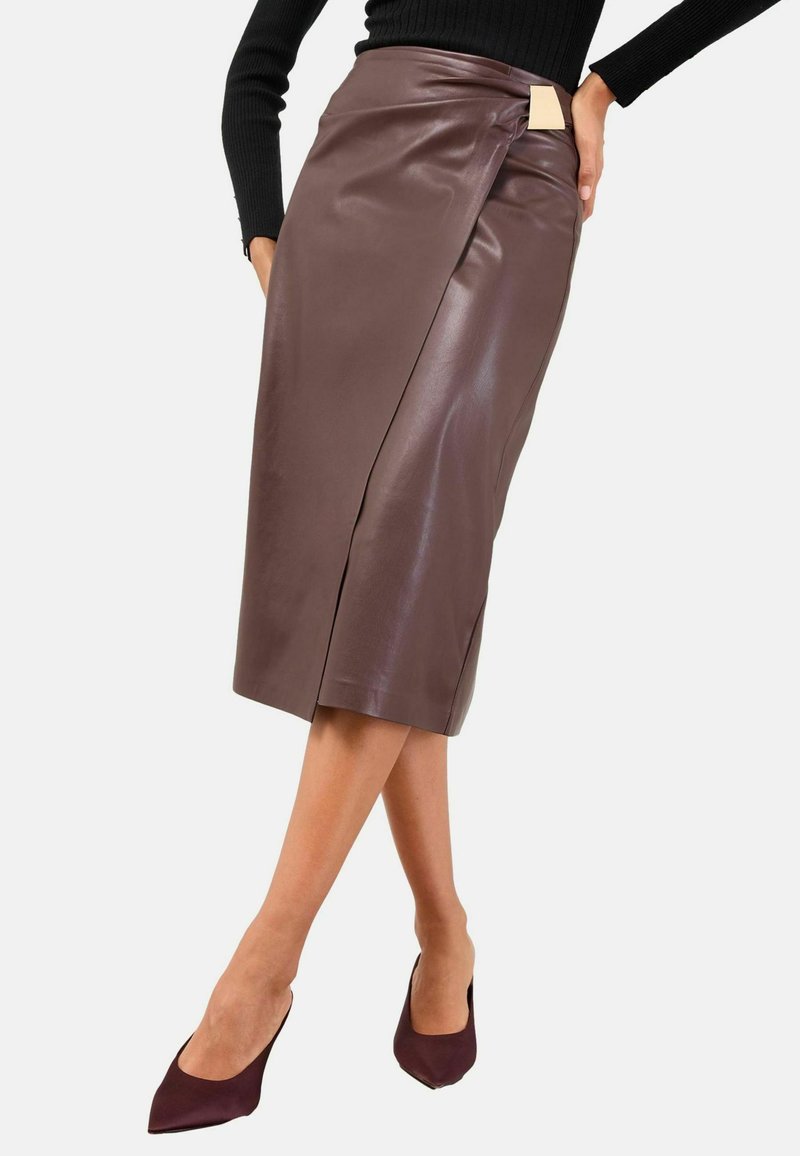 Gonna a matita in pelle marrone con design avvolto, caratterizzata da una spacco laterale e un piccolo dettaglio con etichetta in vita. Texture liscia, lunghezza media.