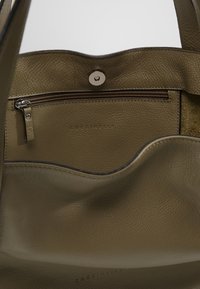 Skórzana torebka w kolorze oliwkowej zieleni o miękkiej fakturze, z centralną kieszenią na zamek, srebrnymi okuciami oraz wytłoczonym logo wewnątrz.