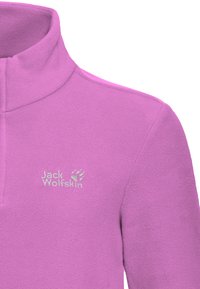 Pile rosa chiaro con collo alto. Presenta un logo argentato "Jack Wolfskin" e un'impronta di zampa sul lato sinistro del petto. Texture liscia.